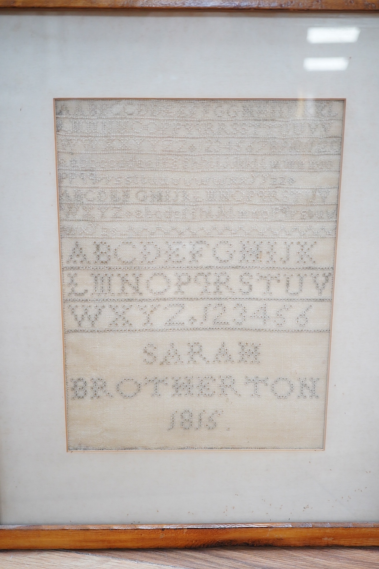 A George III needlework sampler, by Sarah Brotherton, dated 1815, a simple graduated monochrome alphabet sampler, the top worked in fine embroidery stitches, the main part in fine button holestitch around the shapes of c